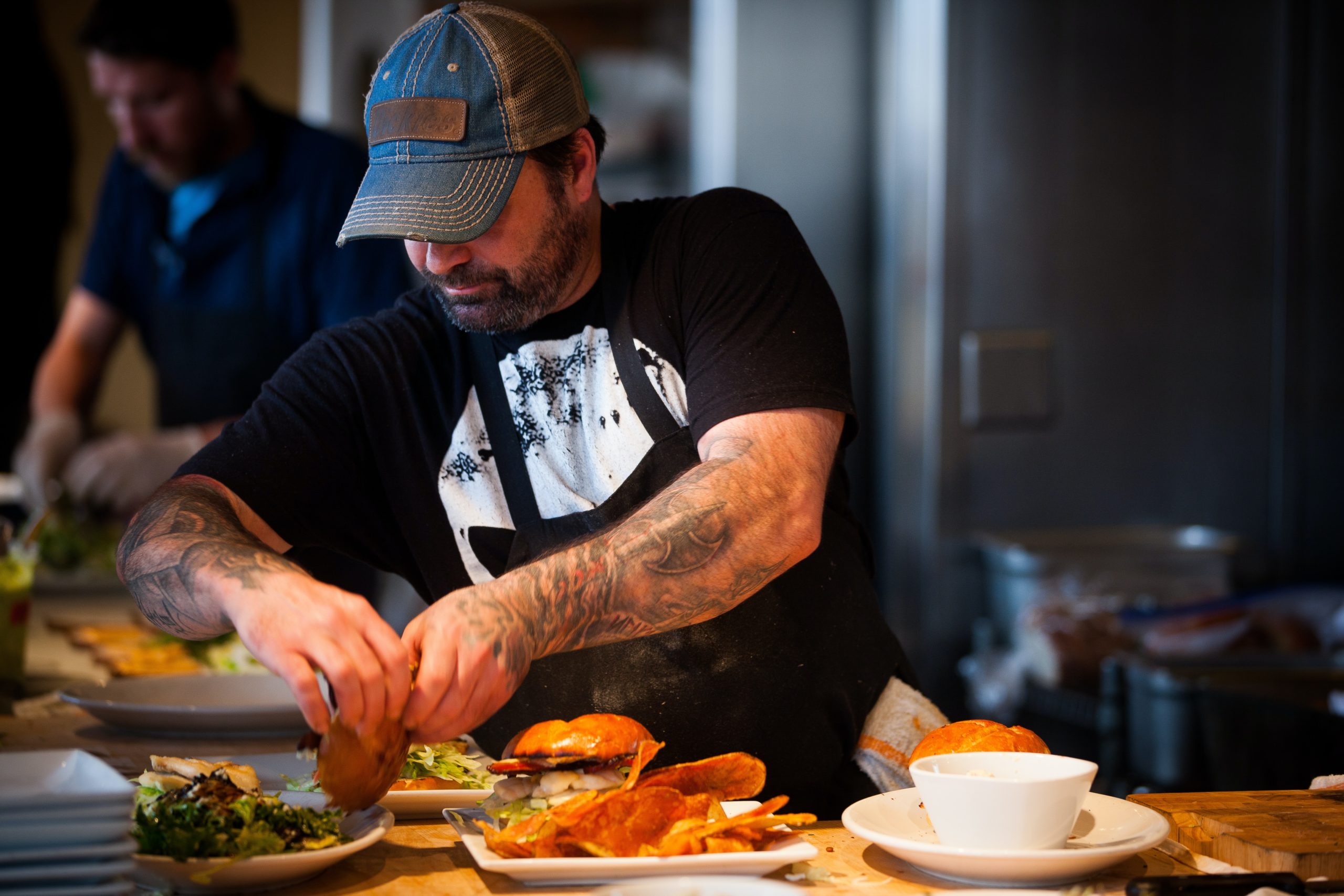 man wearing apron and cap putting together a burger